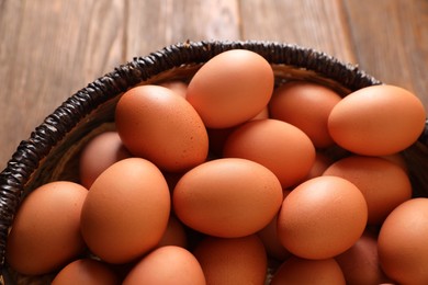 Photo of Raw chicken eggs in wicker basket on wooden table, closeup