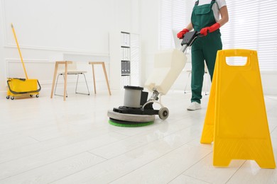 Professional janitor cleaning parquet floor with polishing machine in office, closeup