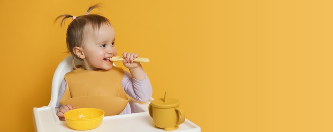 Cute little baby wearing bib while eating on yellow background, space for text. Banner design