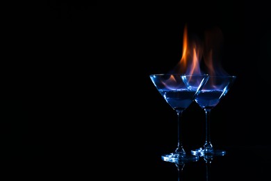 Cocktail glasses with flaming vodka on black background, space for text