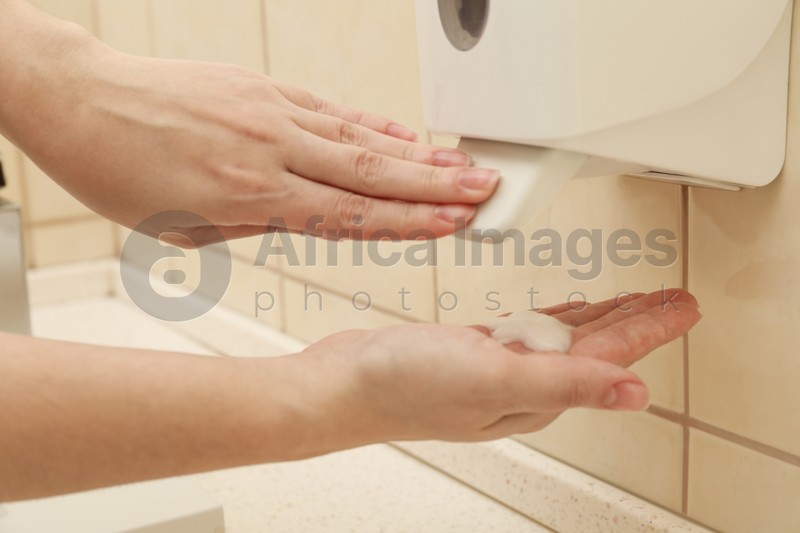 Woman applying antiseptic gel on hand in public bathroom, closeup