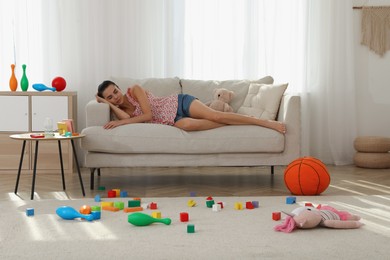 Tired young mother sleeping on sofa in messy living room