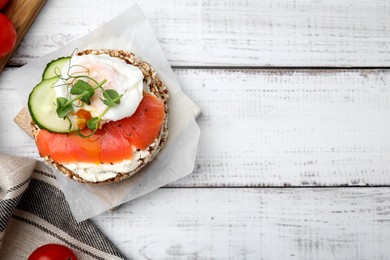 Crunchy buckwheat cakes with salmon, poached egg and cucumber slices on white wooden table, flat lay. Space for text