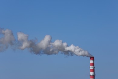 Photo of Polluting air with smoke from industrial chimney outdoors against blue sky. CO2 emissions