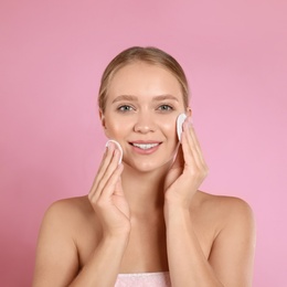 Beautiful young woman with cotton pads on pink background