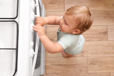 Photo of Little child playing with gas stove indoors, above view. Dangers in kitchen