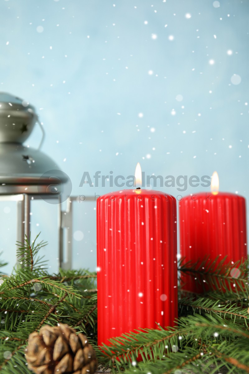 Photo of Snow falling on burning candles and fir branches against light blue background. Christmas eve