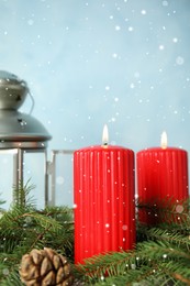 Snow falling on burning candles and fir branches against light blue background. Christmas eve