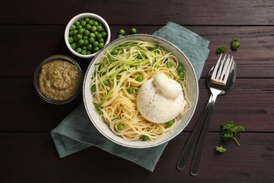 Photo of Bowl of delicious pasta with burrata, peas and zucchini served on wooden table, flat lay