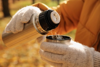 Woman pouring drink from thermos into cap outdoors, closeup