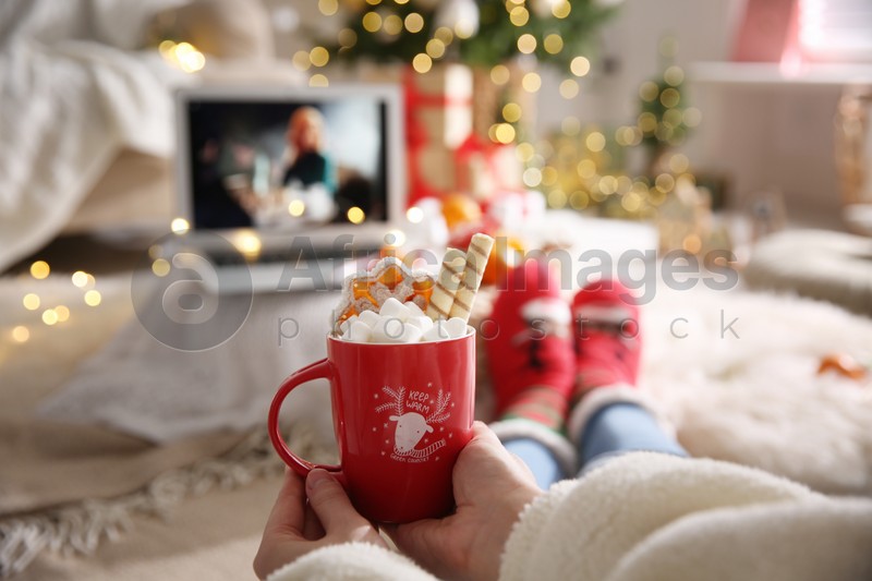 MYKOLAIV, UKRAINE - DECEMBER 25, 2020: Woman with sweet drink watching The Queen's Gambit series on laptop at home, closeup. Cozy winter holidays atmosphere