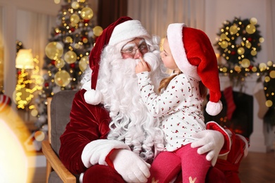 Santa Claus and cute little girl in room decorated for Christmas