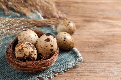Nest and quail eggs on wooden table. Space for text