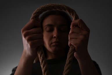 Depressed woman with rope noose on grey background, low angle view