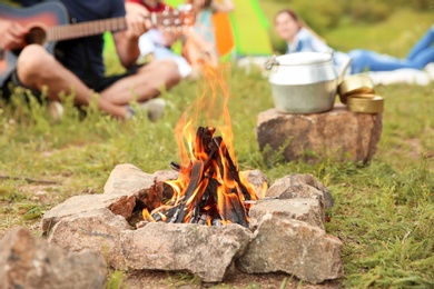 Group of people resting outdoors, focus on bonfire. Camping season