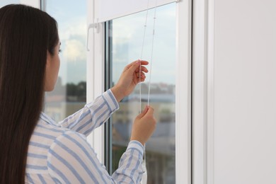 Woman opening white roller blinds on window indoors