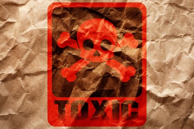 Hazard warning sign (skull-and-crossbones symbol and word TOXIC) on crumpled kraft paper, top view