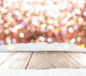 Wooden surface with heap of snow and blurred Christmas lights on background, bokeh effect 