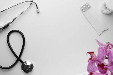 Stethoscope, pills and orchid flower on white background, flat lay with space for text. Women's Health concept