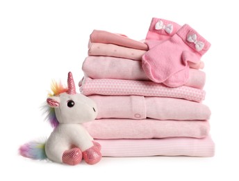 Stack of baby girl's clothes, socks and toy unicorn on white background
