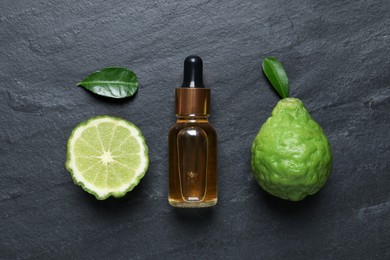 Glass bottle of bergamot essential oil and fresh fruits on black slate table, flat lay