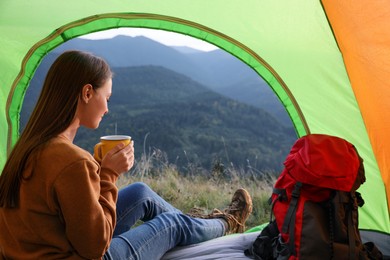 Young woman with drink inside of camping tent in mountains