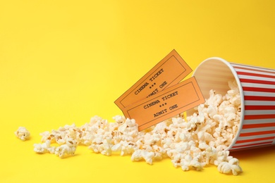 Bucket of fresh popcorn and tickets on yellow background, space for text. Cinema snack