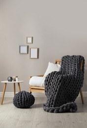 Soft chunky knit blanket on armchair in room. Interior design