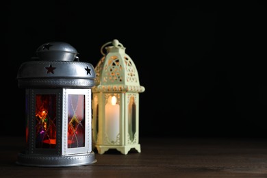 Decorative Arabic lanterns on wooden table against black background, space for text