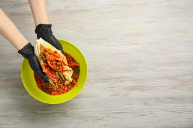 Woman preparing spicy cabbage kimchi at wooden table, top view. Space for text