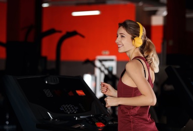 Young woman with headphones listening to music and running on treadmill at gym