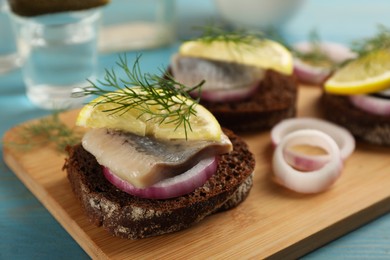 Photo of Delicious sandwiches with pieces of salted herring, lemon, onion rings and dill on light blue wooden table, closeup