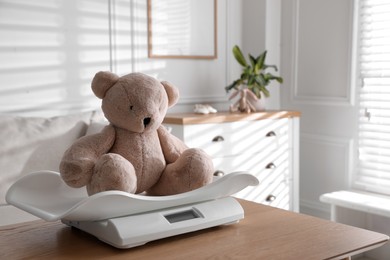 Baby scales with teddy bear on table in room