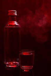 Bottle and glass with vodka on table against red background