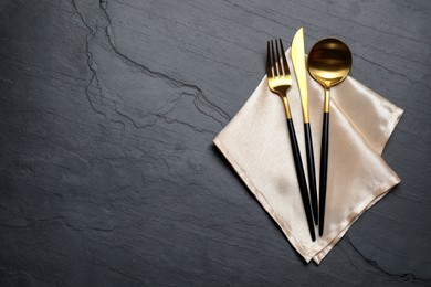Set of golden cutlery with napkin on black table, top view. Space for text