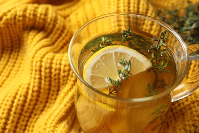 Photo of Fresh thyme tea with pieces of lemon on yellow knitted blanket, closeup