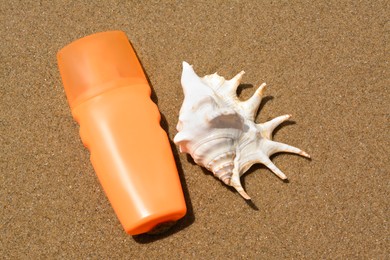 Bottle with sun protection spray and seashell on sandy beach, flat lay