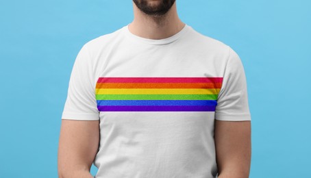 Young man wearing white t-shirt with image of LGBT pride flag on turquoise background, closeup
