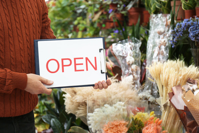Male business owner holding OPEN sign in his flower shop, closeup