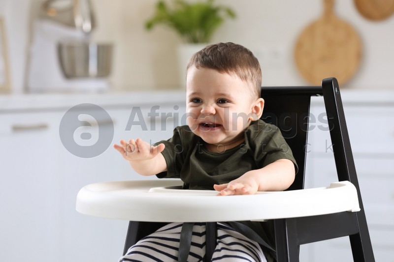 Cute little baby sitting in high chair at kitchen