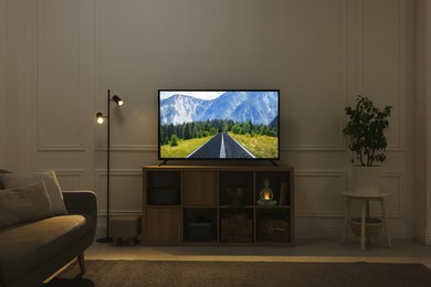 Modern TV set on wooden stand in room. Scene of nature themed movie on screen