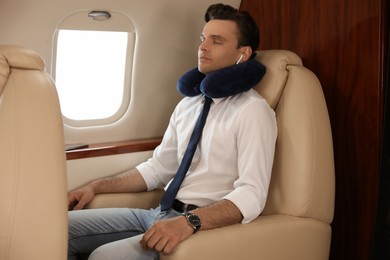 Young man with travel pillow resting while listening to music in airplane during flight