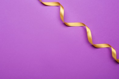 Beautiful golden ribbon on purple background, top view. Space for text