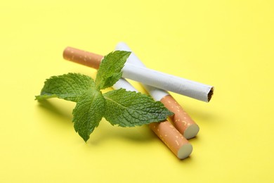 Menthol cigarettes and mint on yellow background
