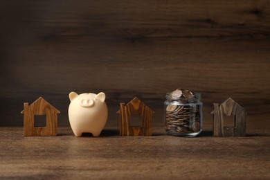 Photo of Piggy bank, jar of coins and house models on wooden table
