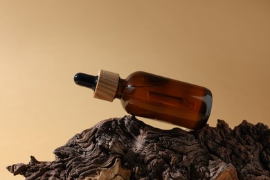 Photo of Bottle of essential oil on tree bark against dark beige background