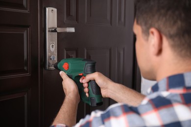 Handyman with screw gun repairing door lock, closeup