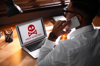 Man in front of laptop with warning about virus attack at workplace