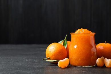 Photo of Composition with tasty tangerine jam on dark table. Space for text