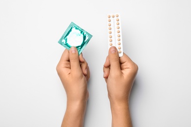 Woman holding condom and birth control pills on white background, top view. Safe sex